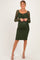 woman wearing a dark green lace maternity dress with long sleeves and a keyhole neckline, showing her baby bump