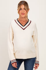 woman wearing a cream v-neck maternity sweater with maroon and navy stripes at the neckline and cuffs