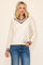 woman wearing a cream v-neck sweater with maroon and navy stripes on the collar and cuffs, paired with blue jeans