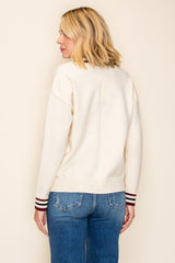 woman wearing a cream colored sweater with striped cuffs and blue jeans, shown from the back