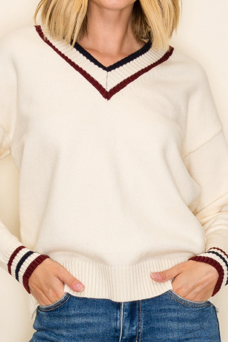 woman wearing a cream v-neck sweater with maroon and navy stripes on the collar and sleeves, styled with blue jeans