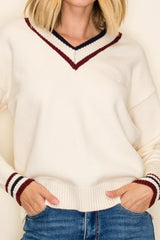 woman wearing a cream v-neck sweater with maroon and navy stripes on the collar and sleeves, styled with blue jeans