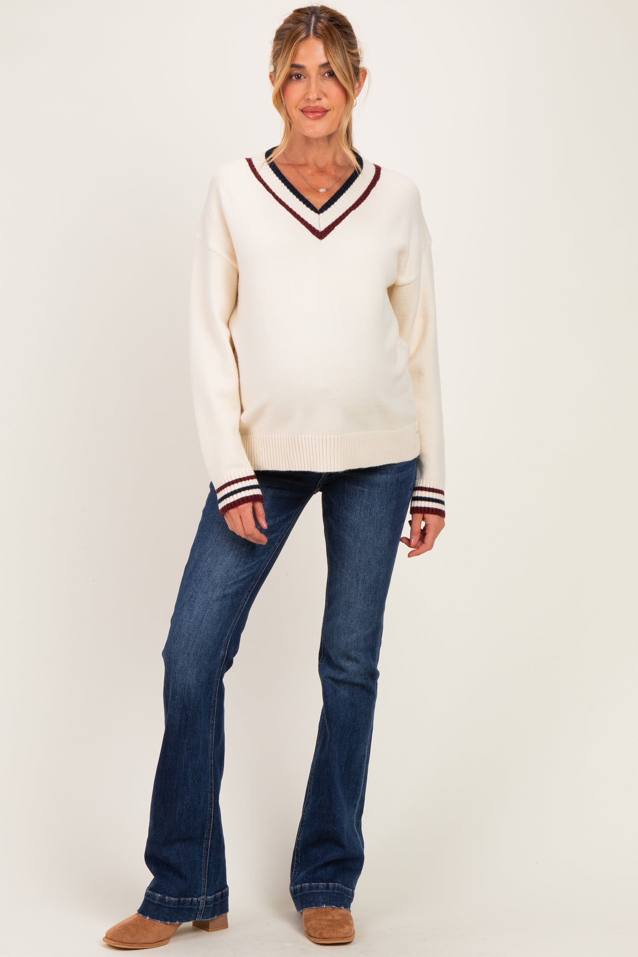 woman wearing a cream v-neck maternity sweater with burgundy and navy stripes, paired with blue flared jeans