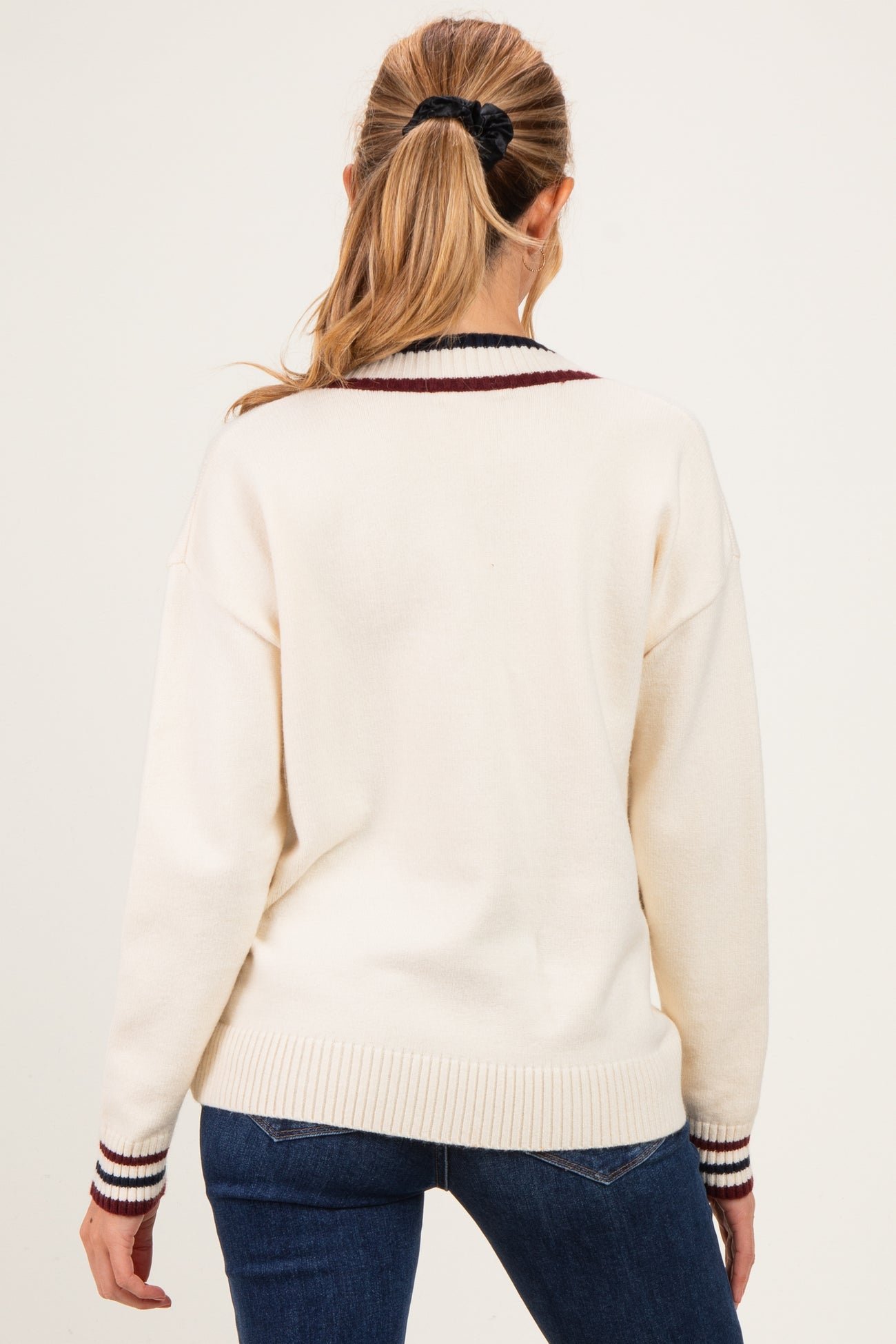 woman wearing a cream-colored maternity sweater with maroon and navy striped detailing on the collar and cuffs