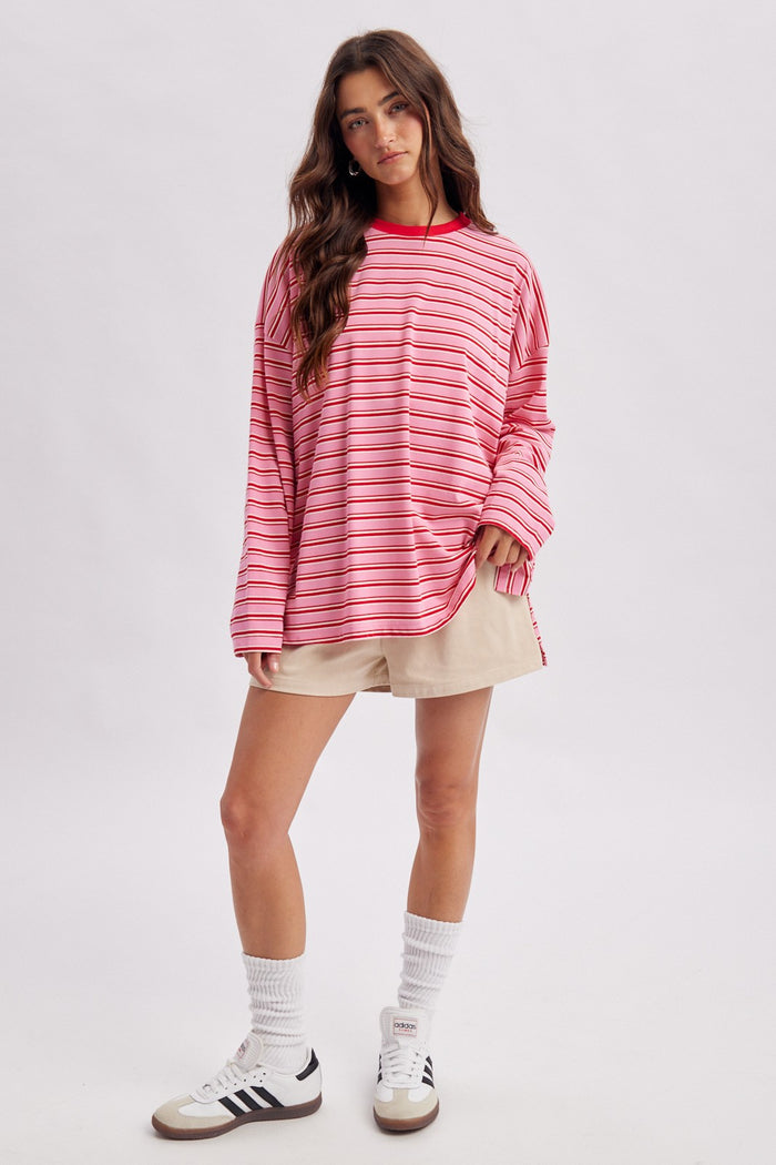 woman wearing a red and pink striped oversized sweatshirt with a crew neck, paired with beige shorts and white socks