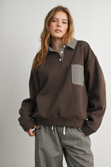 woman wearing a dark brown oversized sweatshirt with a checkered collar and pocket, paired with checkered pants