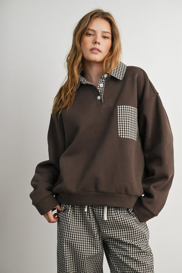 woman wearing a dark brown oversized sweatshirt with a checkered collar and pocket, paired with checkered pants