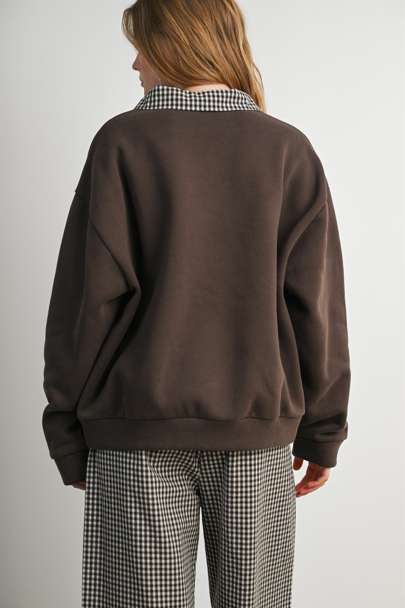 woman wearing a brown oversized sweatshirt with a checked collar, styled with checked pants