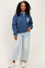 woman wearing a navy blue sweatshirt with a checkered pocket and light wash wide-leg jeans, smiling