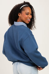 woman wearing a blue oversized sweatshirt layered over a plaid collared shirt, looking back and smiling