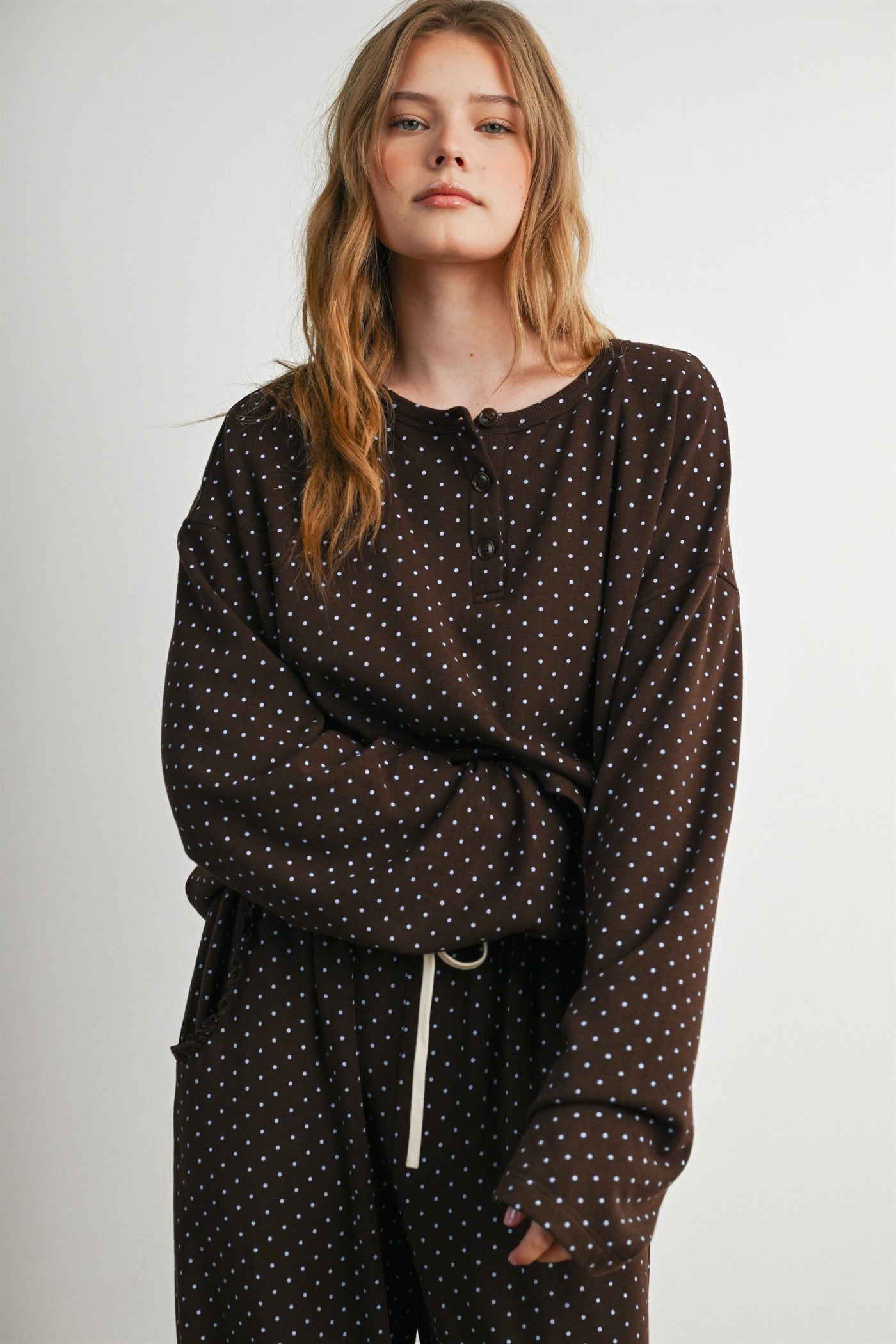 woman wearing a brown polka dot long sleeve top with a henley neckline and relaxed fit