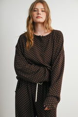woman wearing a brown polka dot long sleeve top with a henley neckline and relaxed fit