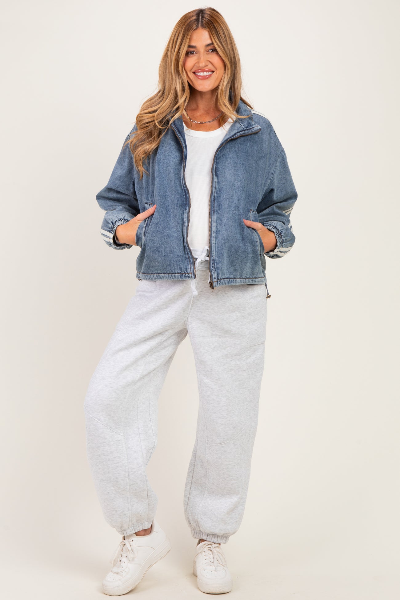 woman wearing a denim zip-up jacket over a white top and gray sweatpants, styled for maternity wear