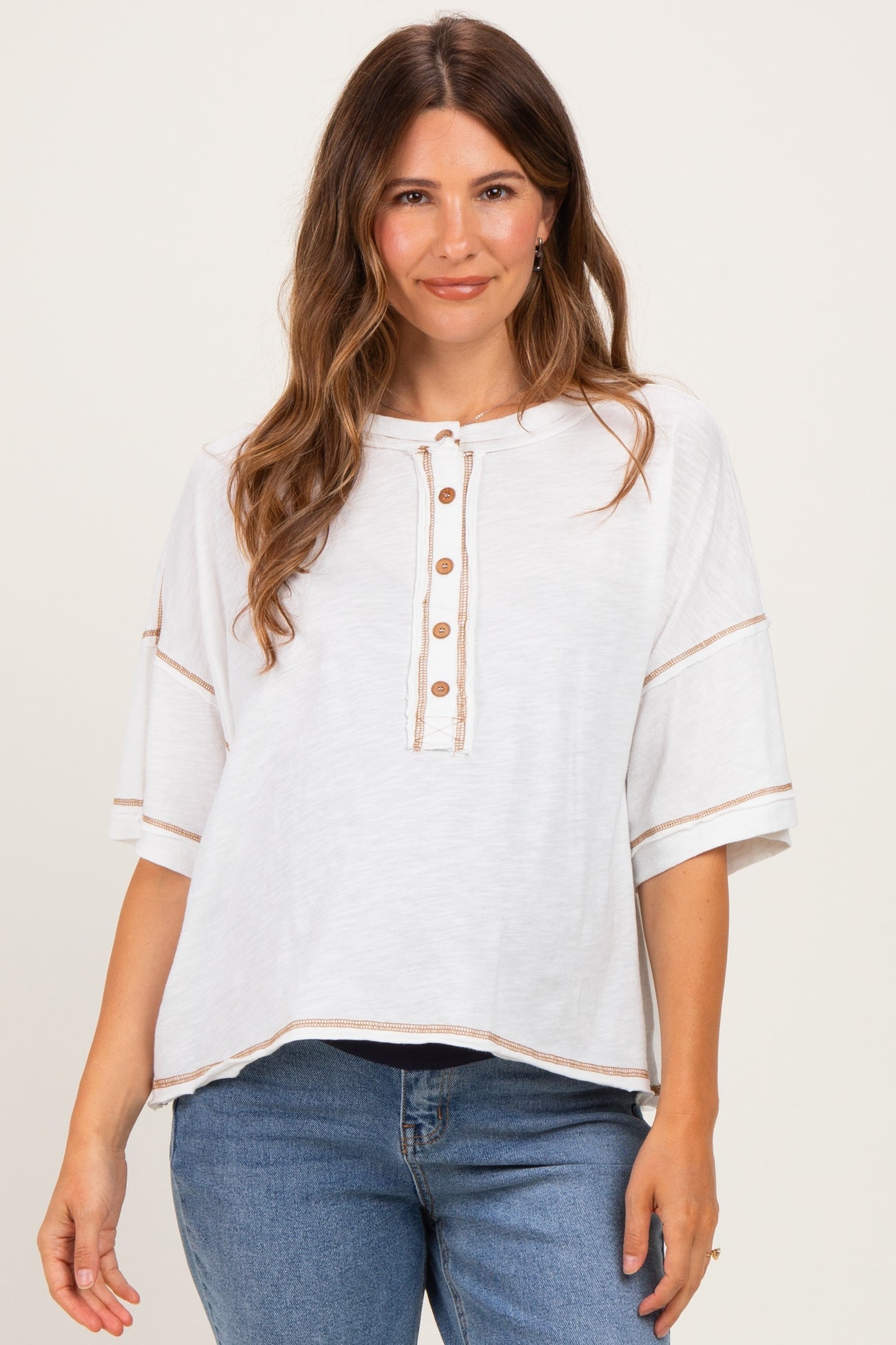 woman wearing a white maternity top with button details and short sleeves, styled with denim jeans