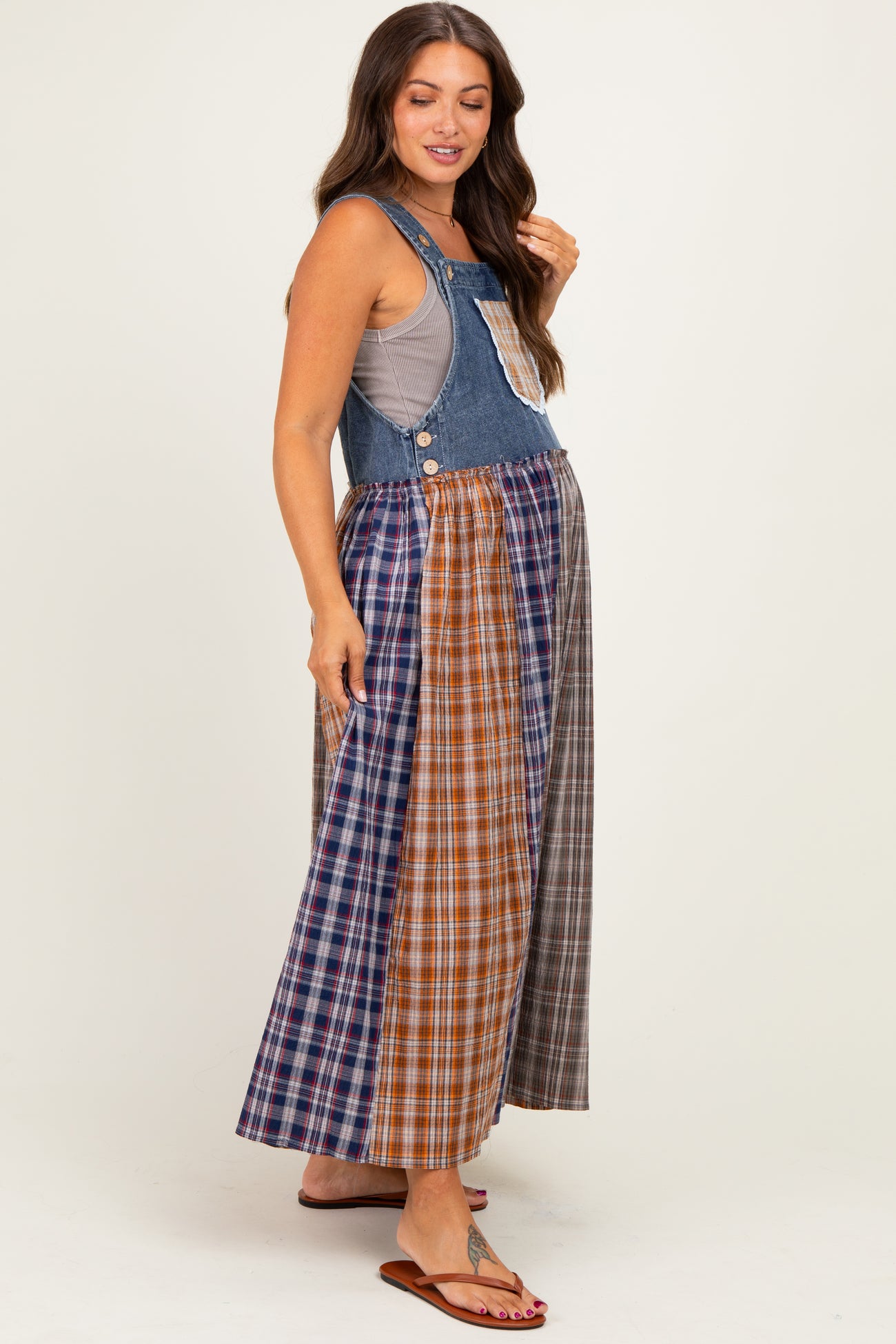 woman wearing a denim maternity maxi dress with a patchwork plaid skirt and a sleeveless top, showing her baby bump