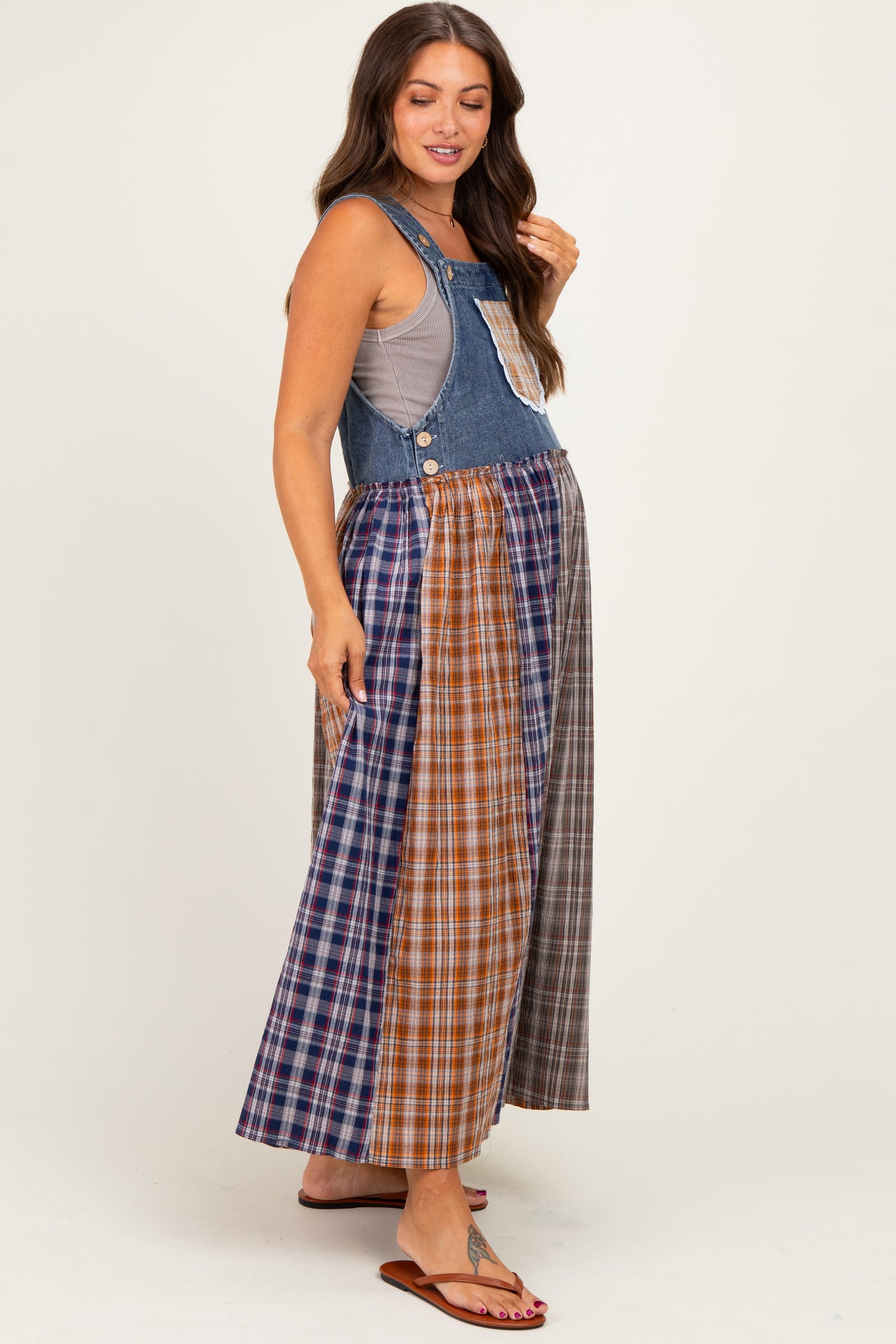 woman wearing a denim maternity maxi dress with a patchwork plaid skirt and a sleeveless top, showing her baby bump
