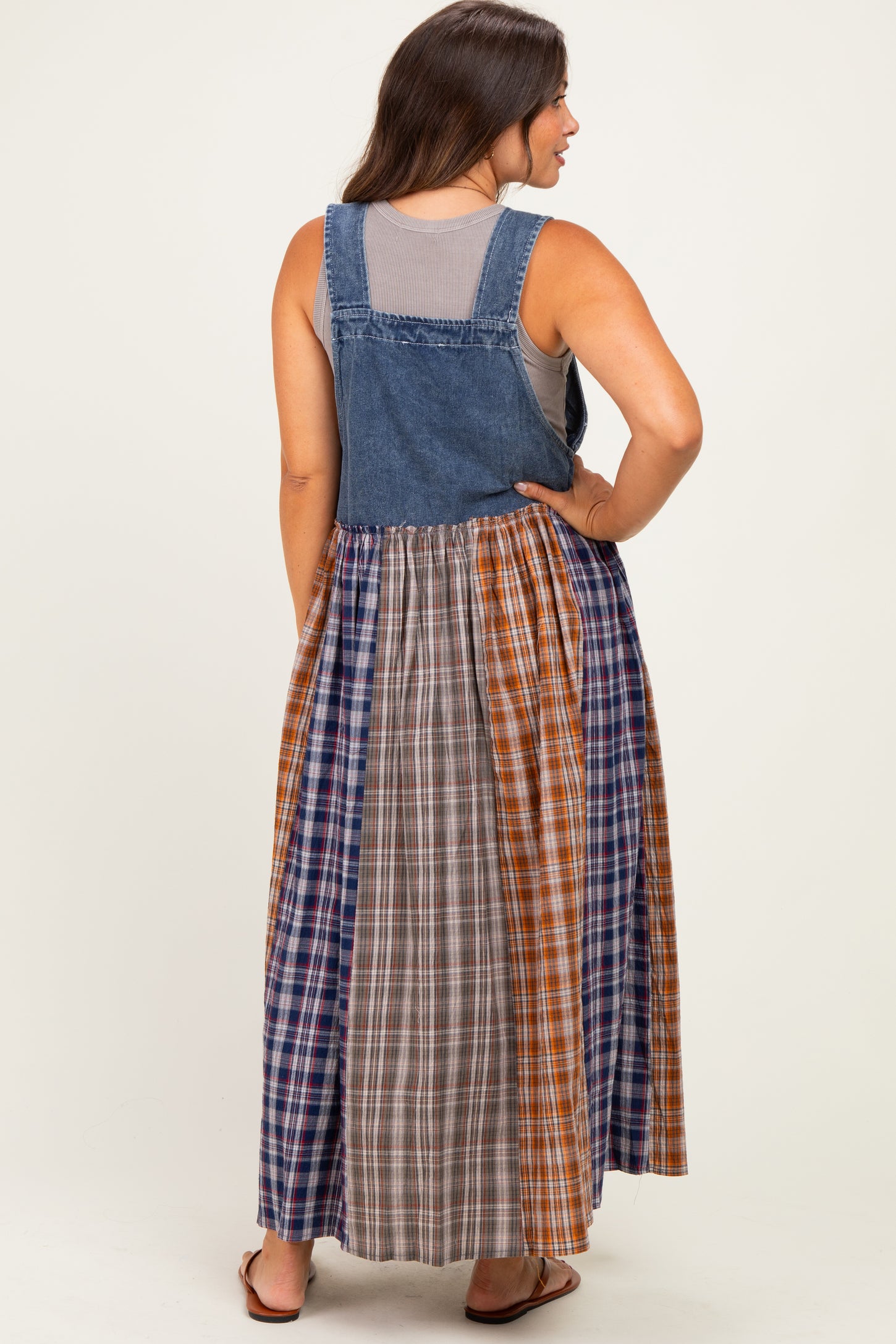 woman wearing a denim maternity maxi dress with a plaid skirt and a gray tank top underneath