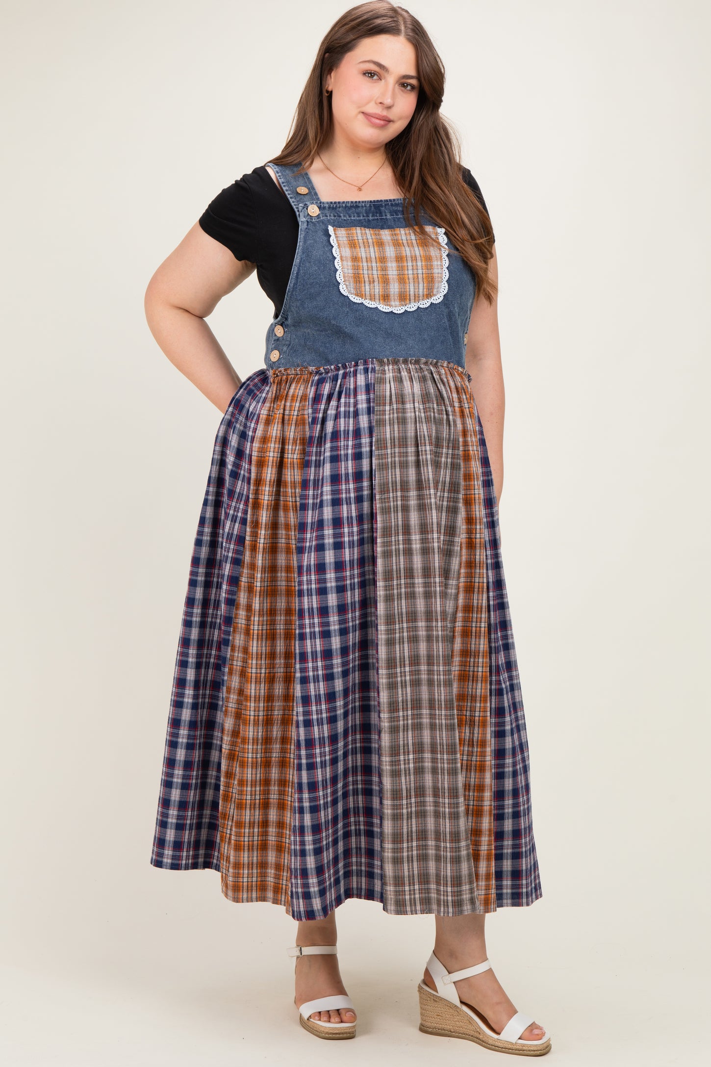 woman wearing a denim maternity plus dress with a plaid skirt and a lace-trimmed bib, no visible baby bump