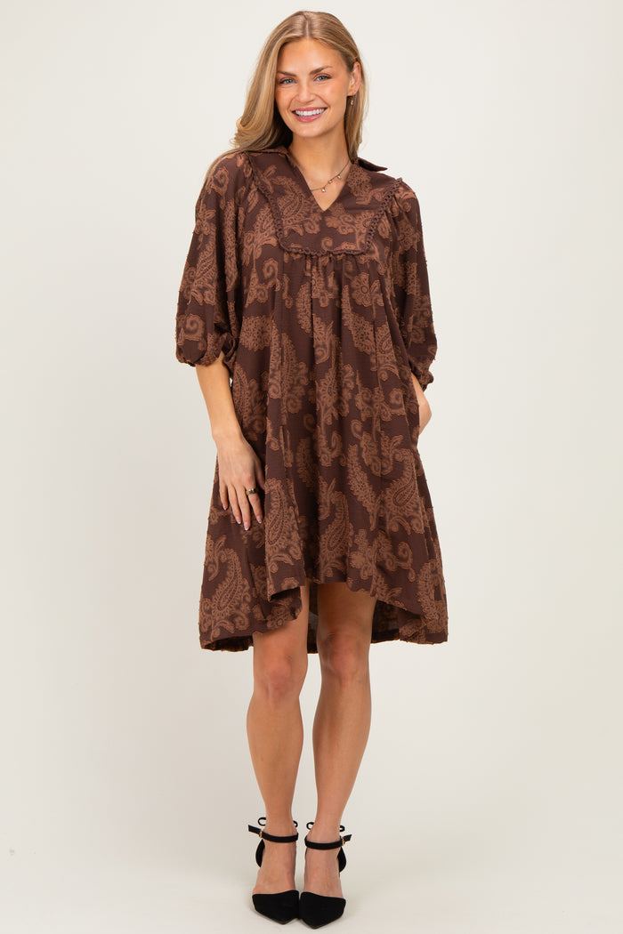 woman wearing a brown paisley print short sleeve dress with a v-neck and slight hi-low hemline