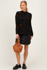woman wearing a black long sleeve top with floral print and a black denim skirt, holding a brown handbag