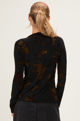 woman wearing a black long sleeve top with a floral print in shades of brown and gold, seen from the back