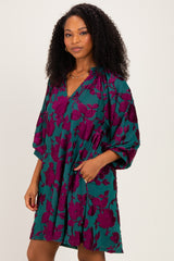 woman wearing a teal floral print tunic dress with deep purple flowers and pockets, styled with a relaxed fit