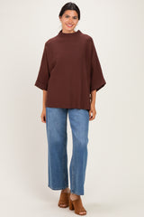 woman wearing a brown oversized top with half sleeves and high-waisted blue wide-leg jeans