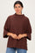 woman wearing a brown oversized sweater with a high neckline and wide sleeves, standing against a light background
