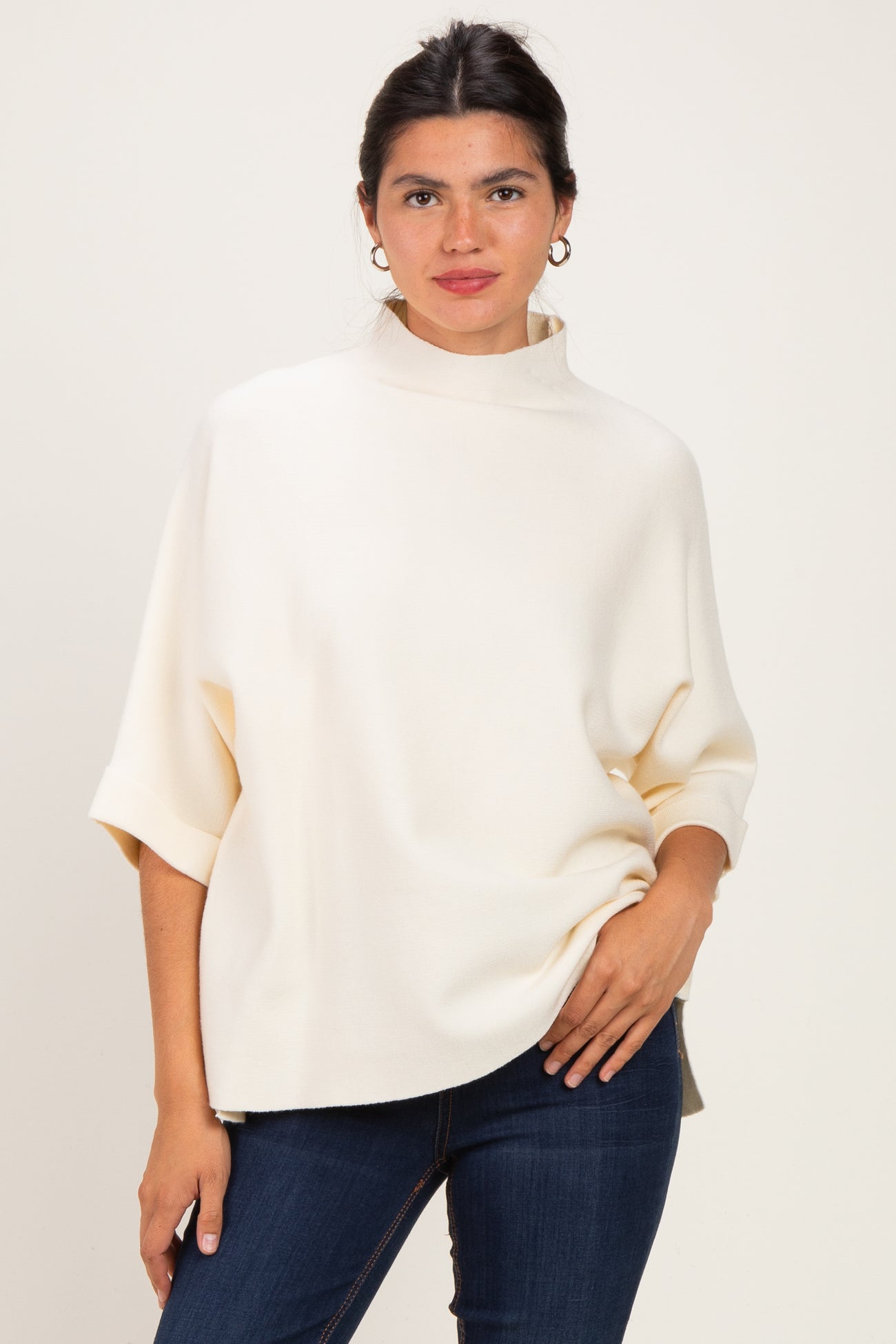woman wearing a cream oversized pullover with a high neckline and rolled sleeves paired with blue jeans