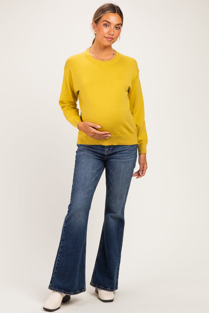 woman wearing a mustard yellow maternity sweater and flared jeans, holding her baby bump