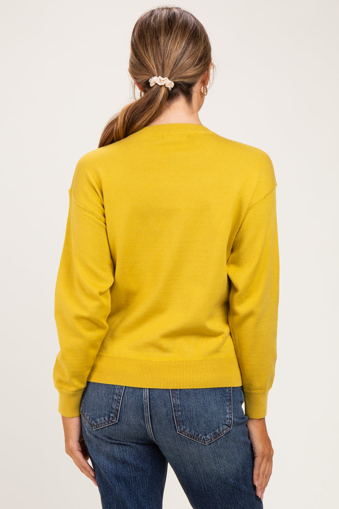 woman wearing a mustard yellow maternity sweater with a relaxed fit and ribbed detailing, styled with blue jeans