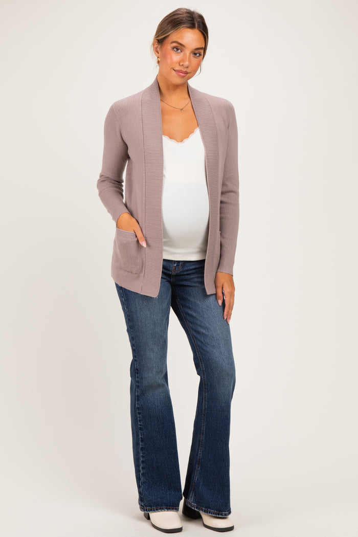 woman wearing a light mauve maternity cardigan over a white top and blue flared jeans, showing her baby bump