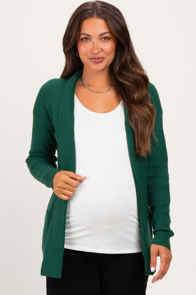 woman wearing a dark green ribbed maternity cardigan over a white shirt, showing her baby bump