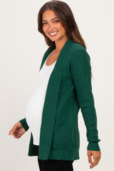 woman wearing a green open-front maternity cardigan over a white tank top and showing her baby bump