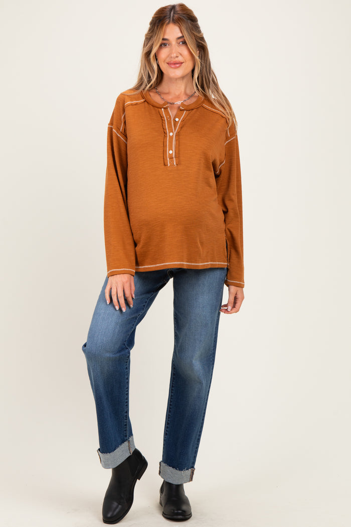 woman wearing a rust-colored maternity top with a button detail and paired with relaxed denim jeans