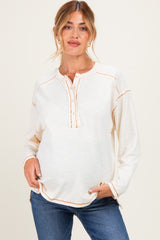 woman wearing a cream maternity top with a henley neckline and orange stitching, showing her baby bump