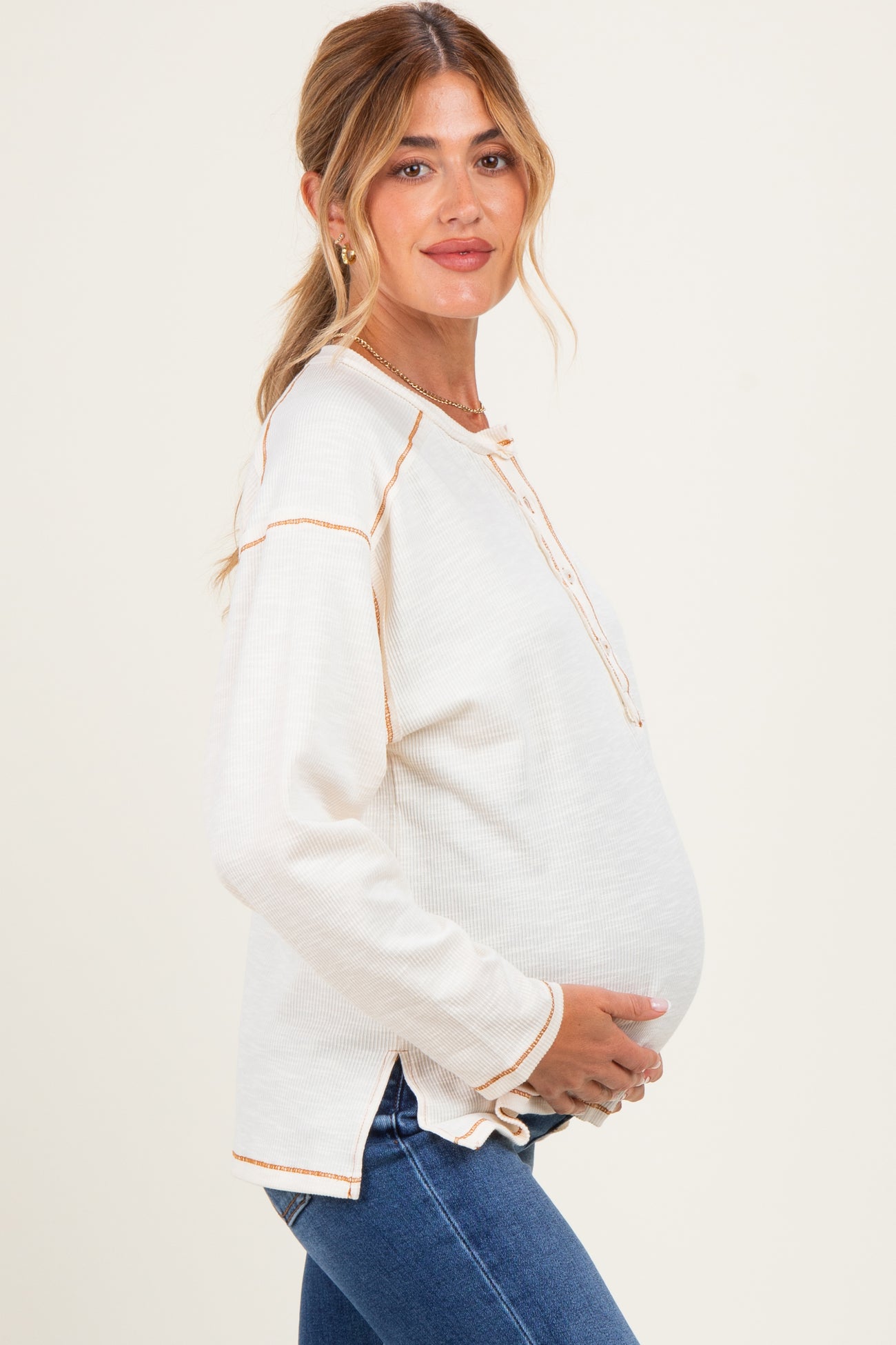 woman wearing a cream long sleeve maternity top with button details and holding her baby bump