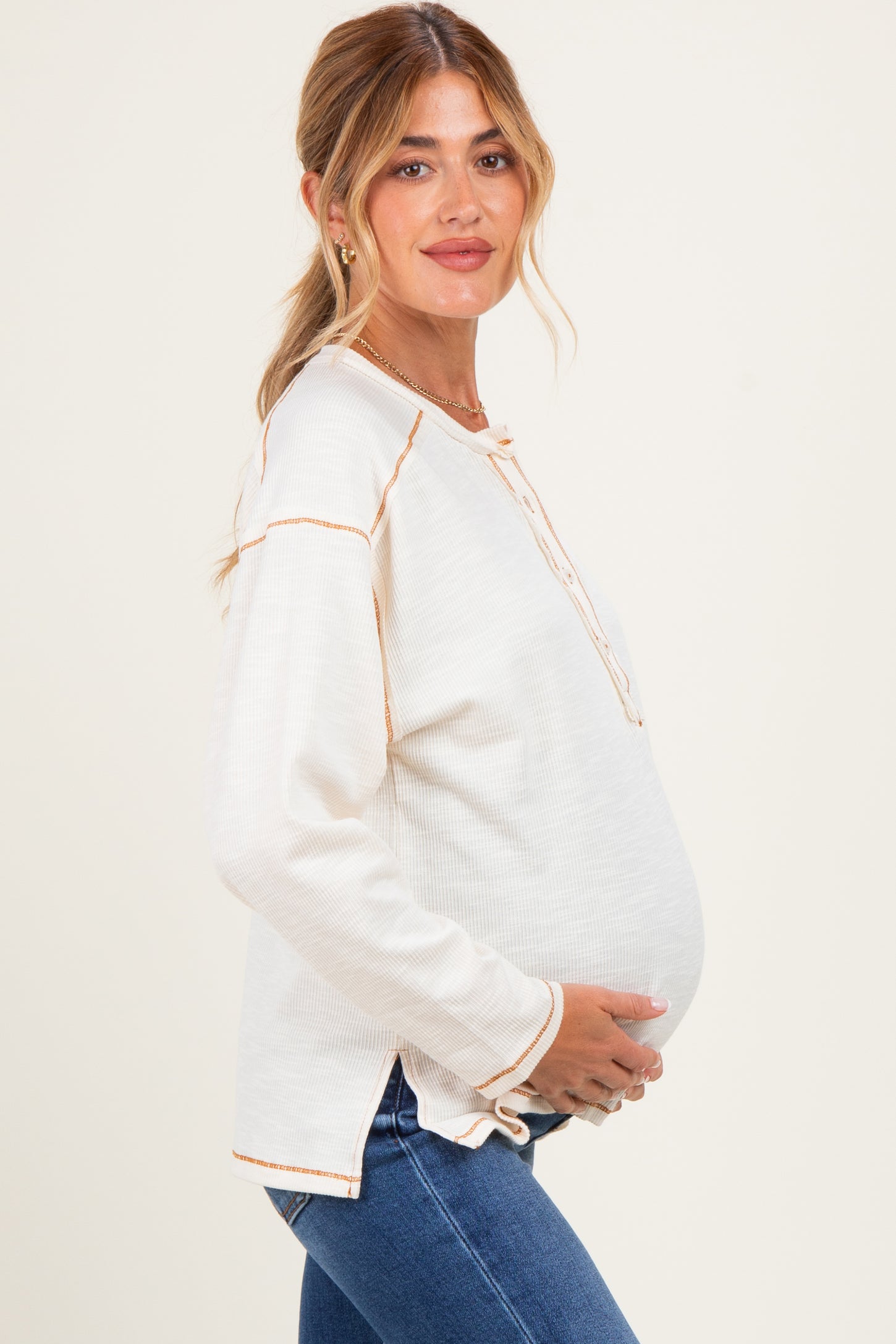 woman wearing a cream long sleeve maternity top with button details and holding her baby bump