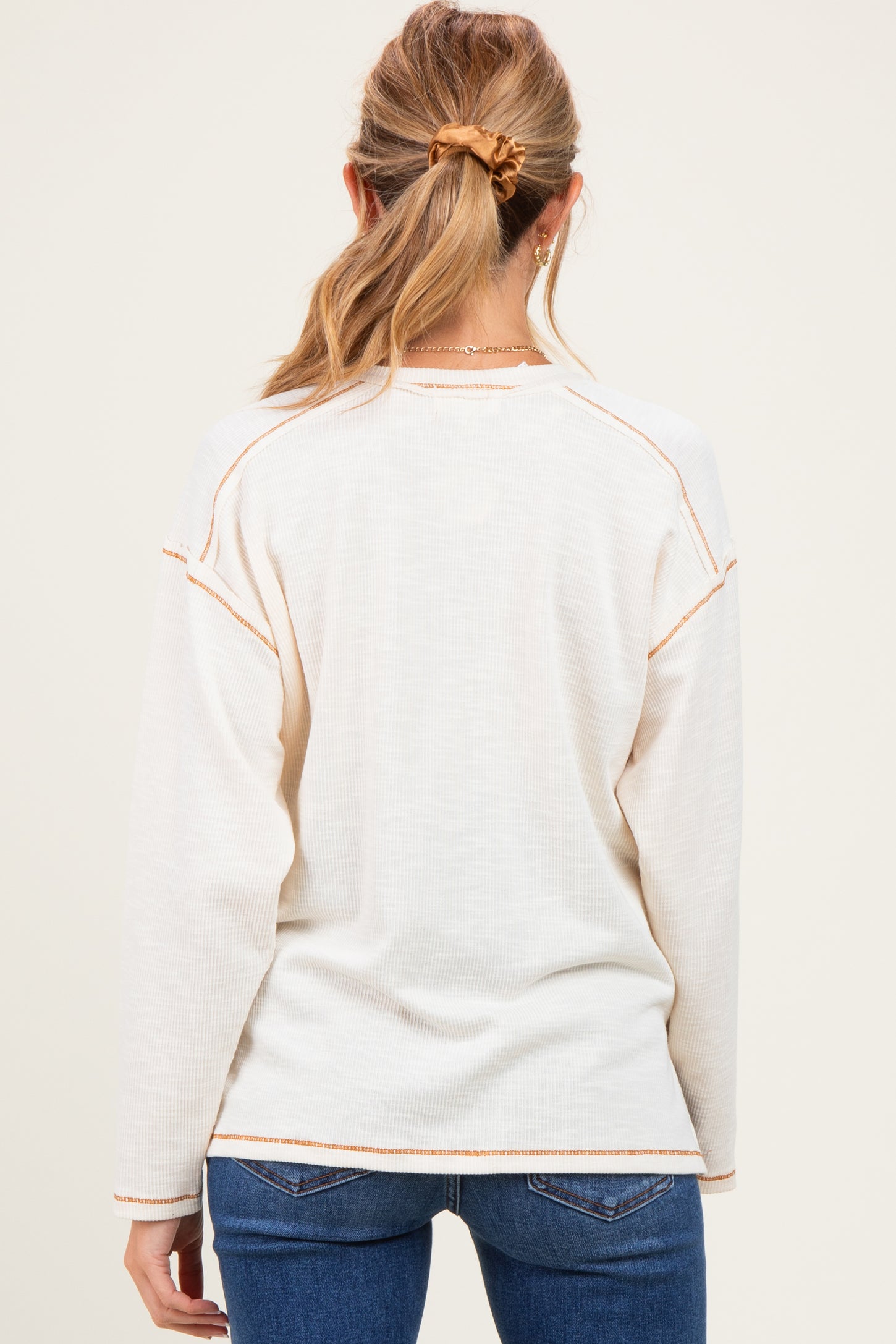 woman wearing a cream maternity sweater with contrasting stitch details, shown from the back