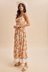 woman wearing a brown floral maxi dress with spaghetti straps and a white hem, accessorized with a wide-brimmed hat