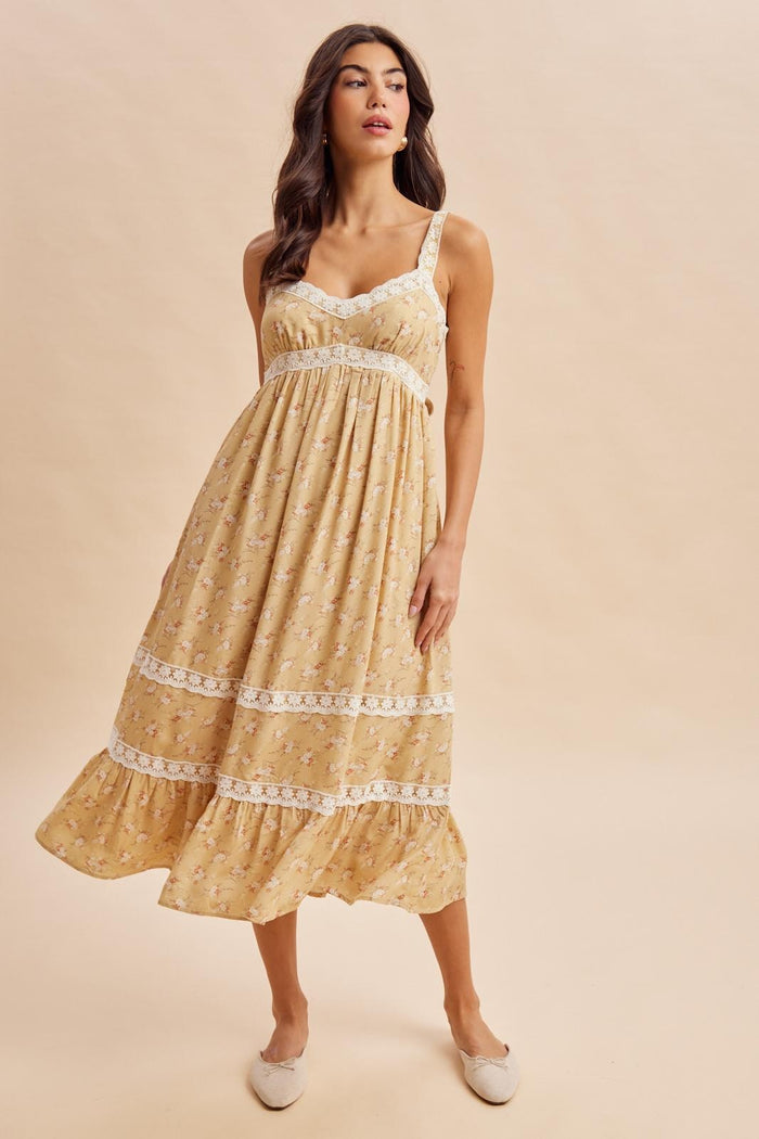 woman wearing a yellow floral sundress with lace detailing and a flared hem, standing against a neutral background