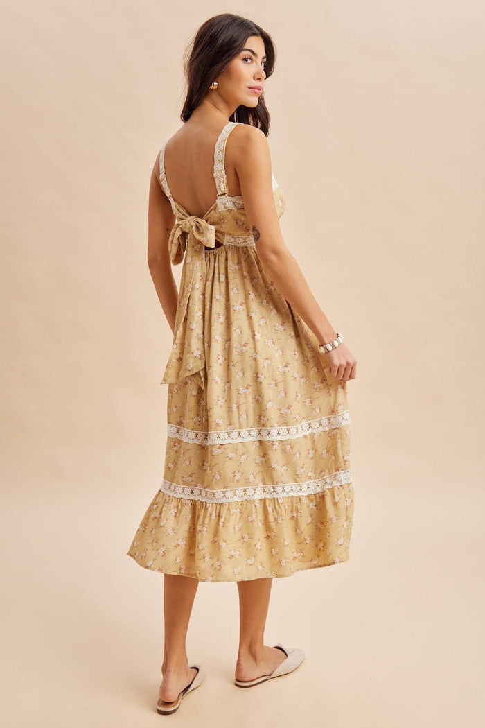 woman wearing a yellow floral maxi dress with lace trim and a bow detail at the back