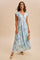 woman wearing a light blue floral maxi dress with flutter sleeves, posing with a small handbag