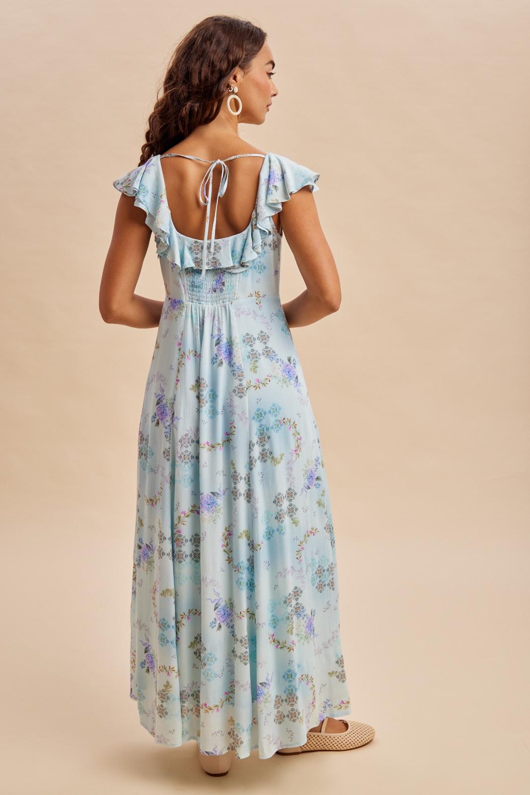 woman wearing a light blue floral maxi dress with ruffled sleeves and an open back detail, viewed from the back