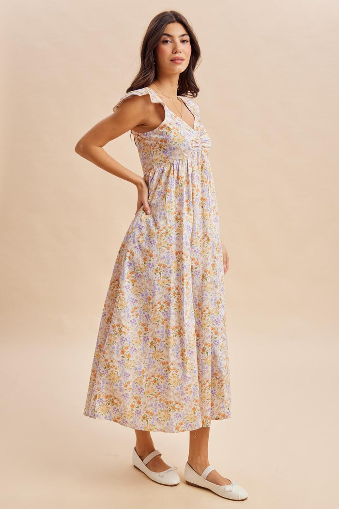 woman wearing a floral maxi dress with ruffle straps and a cinched waist, standing in profile on a neutral background