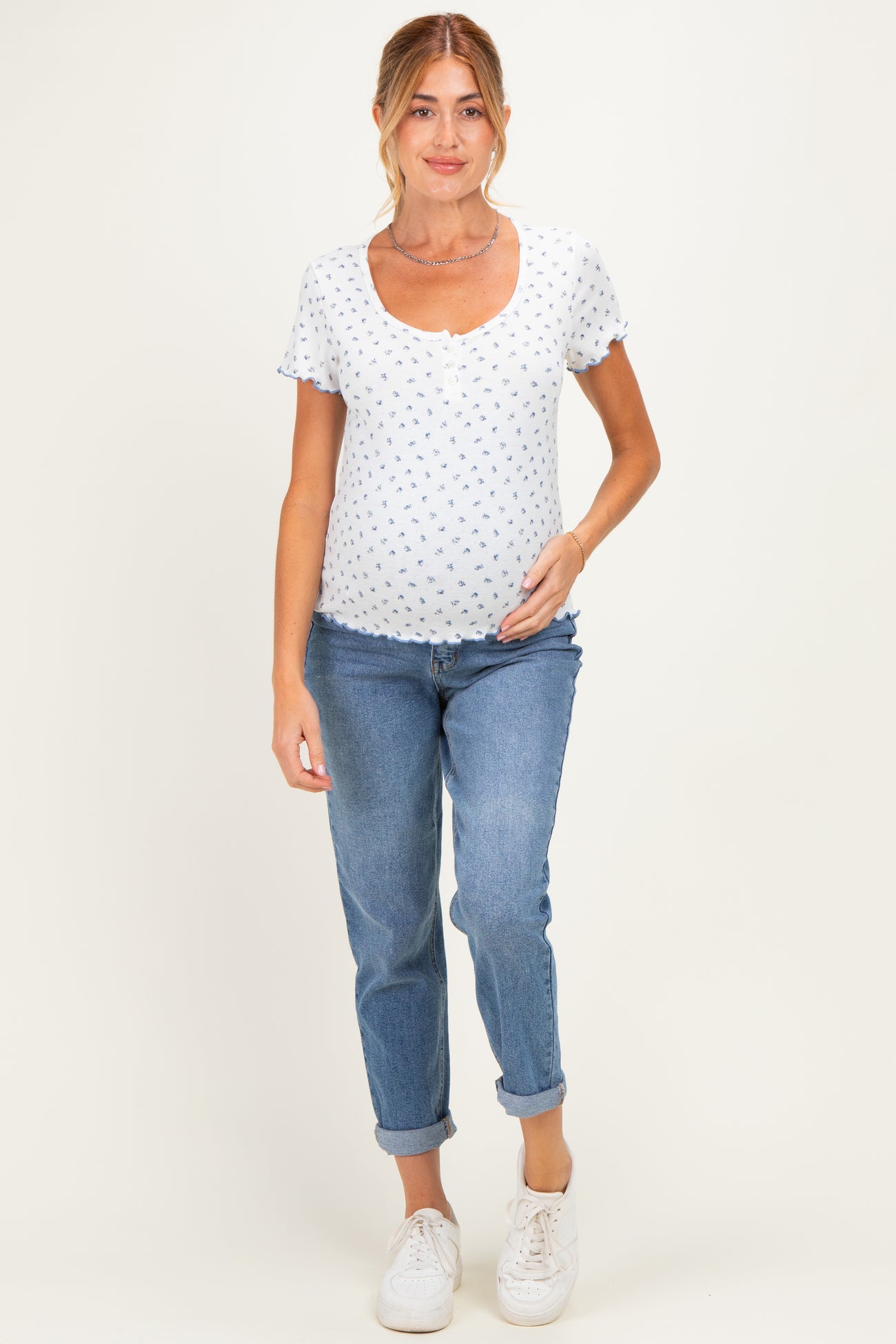 woman wearing a white maternity top with blue floral prints and blue jeans, showcasing her baby bump