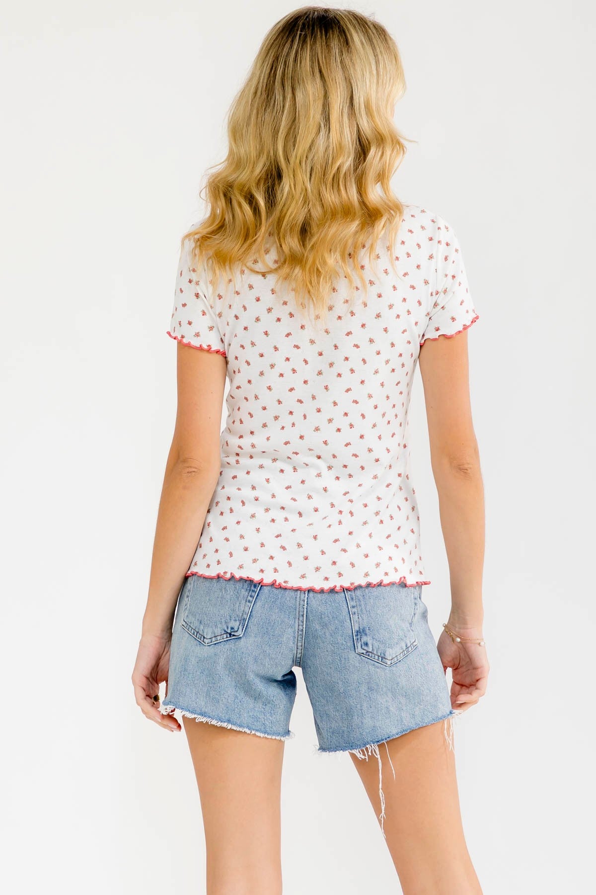 woman wearing a white short sleeve top with pink floral print and frayed denim shorts, viewed from the back