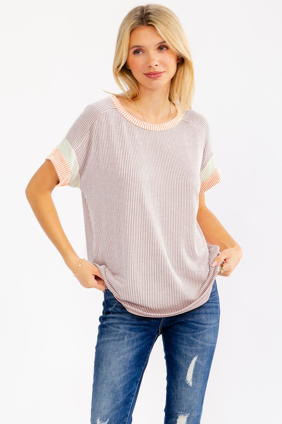 woman wearing a striped short sleeve top with pastel color blocking and distressed blue jeans