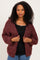 woman wearing a maroon open front chunky knit cardigan over a black tank top and blue jeans