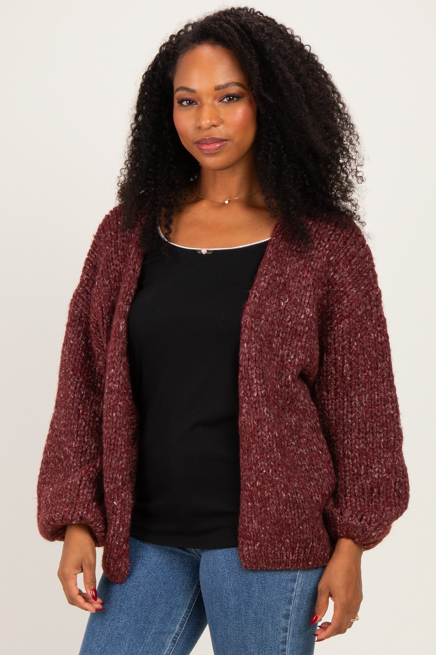 woman wearing a burgundy chunky knit cardigan over a black top and blue jeans